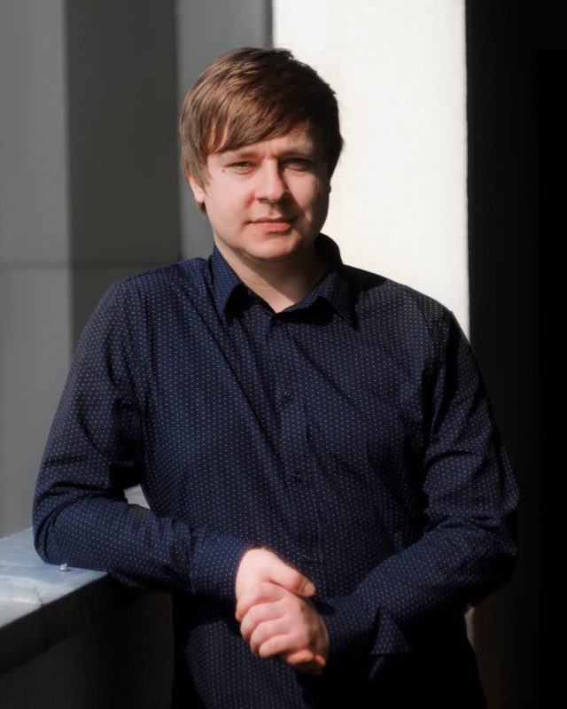 Mateusz Małys standing in a sunlit hallway, arms resting on a ledge